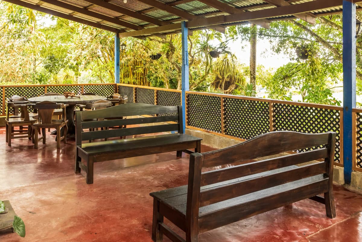 Corredor y terraza exterior con bancas de madera rústica y mesa redonda para comensales