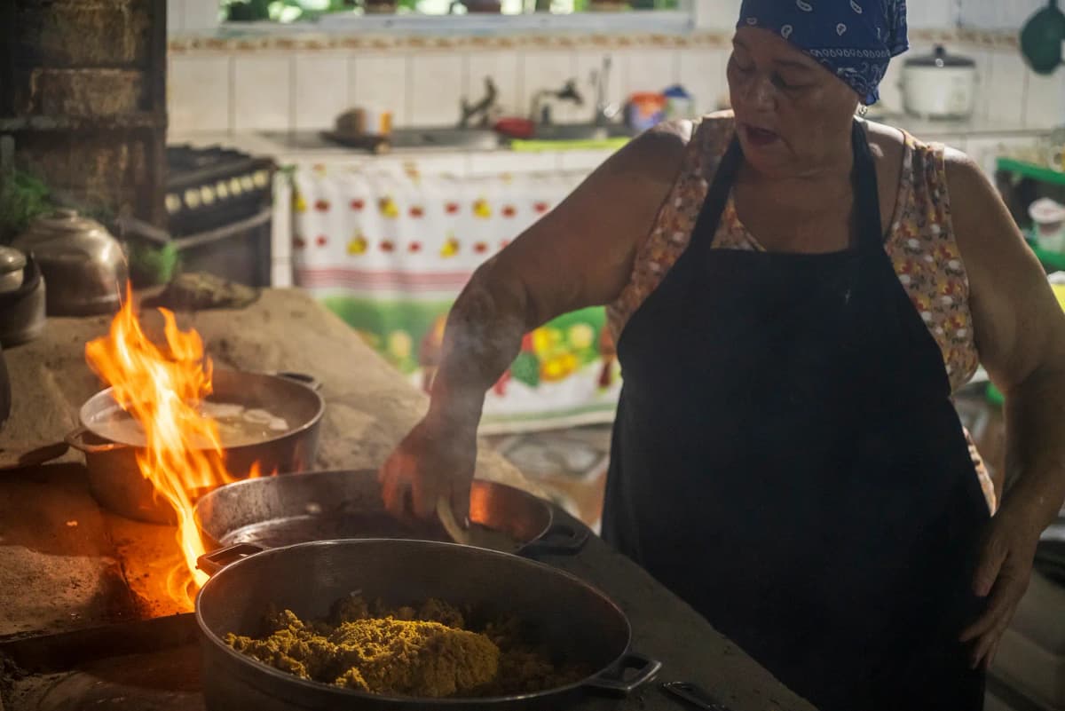 Cocinera tradicional preparando alimentos en el fogón de leña con llamas vivas