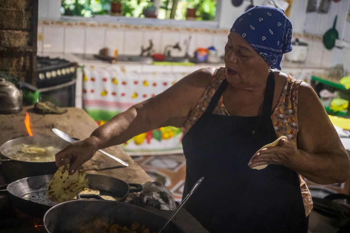 Cocinera tradicional palmeando y cocinando tortillas de maíz al fuego de leña