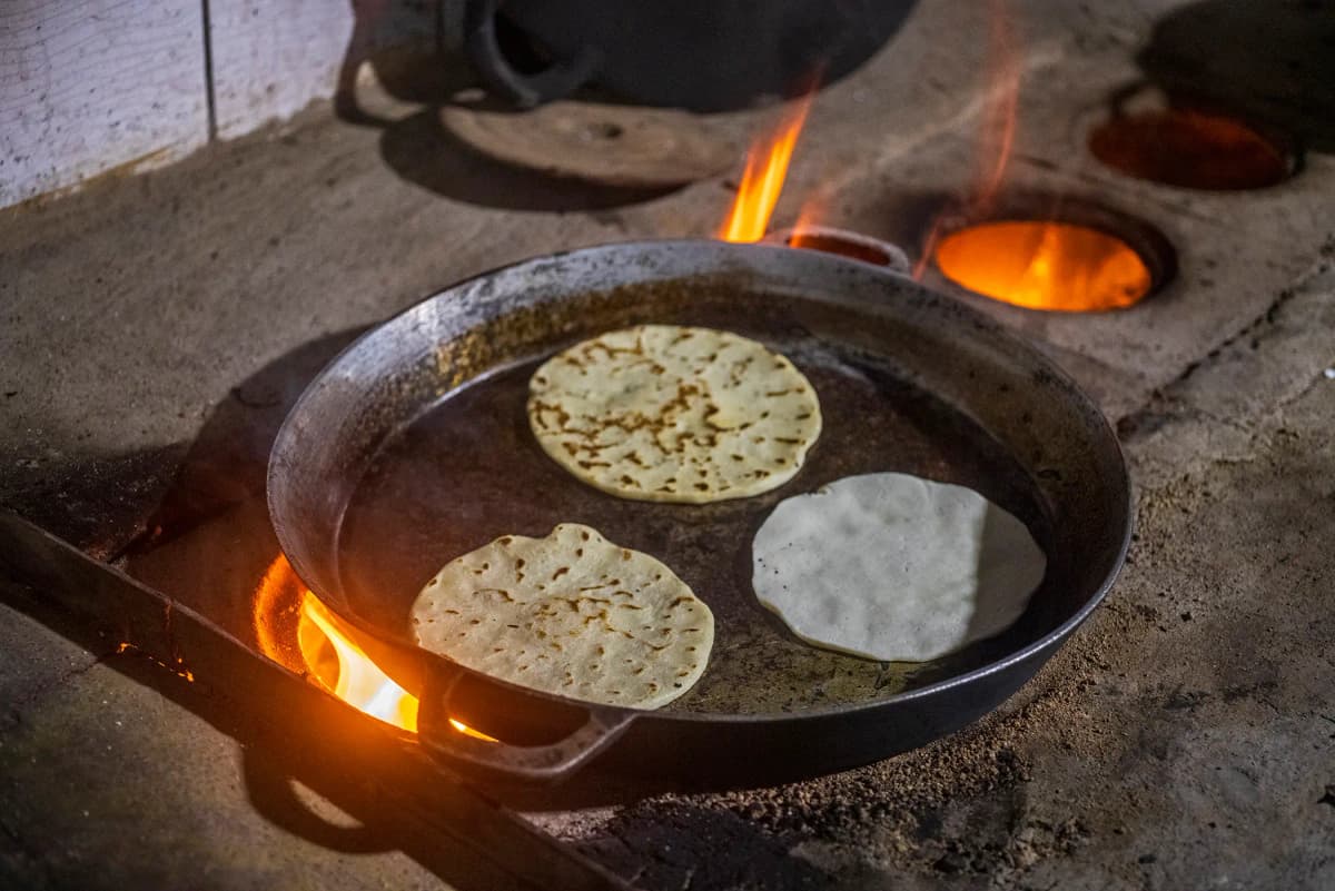 Tortillas de maíz artesanal cociéndose en sartén de hierro al fuego de leña