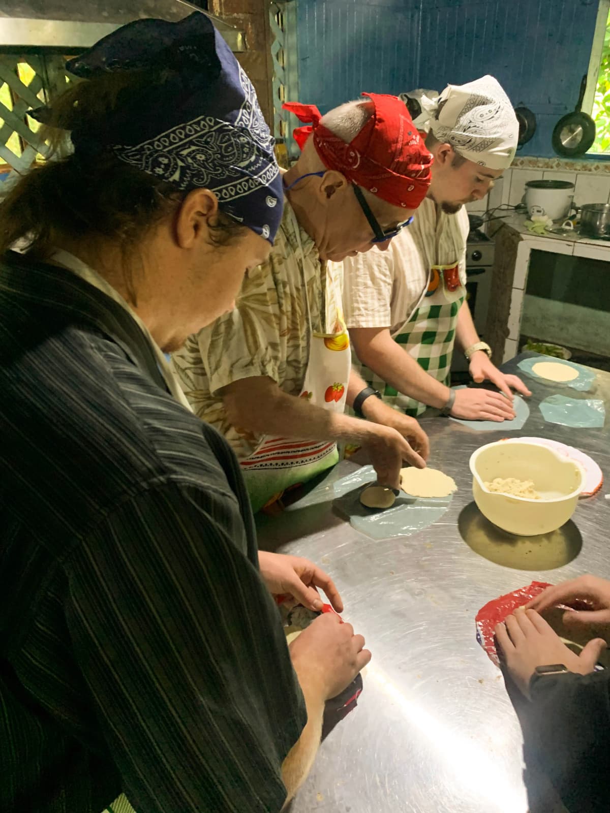 Turistas con pañuelos y delantales palmeando tortillas de maíz en el taller práctico