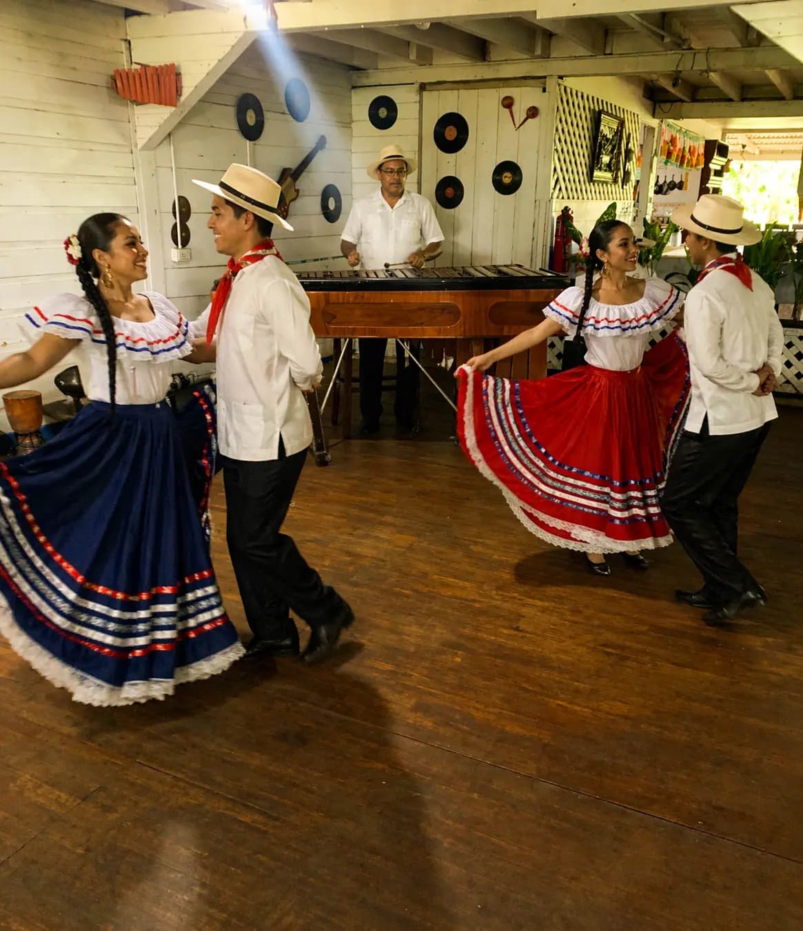 Parejas de bailarines con trajes folclóricos costarricenses realizando una presentación con marimba en vivo