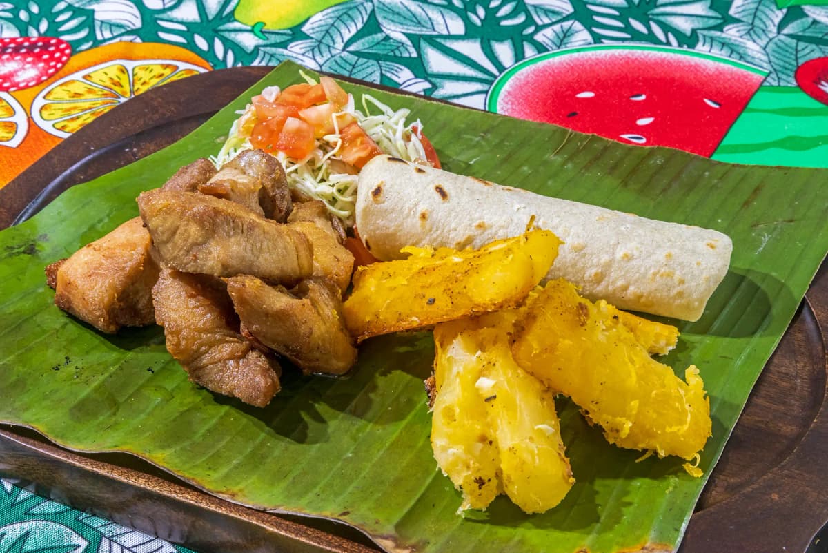 Plato de chicharrón de cerdo tradicional con yuca frita, ensalada fresca y tortilla